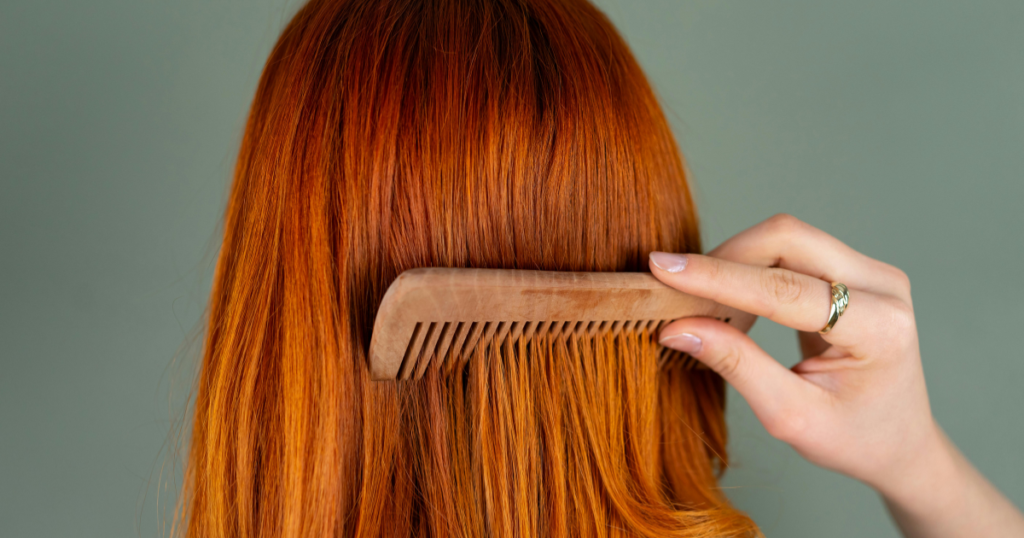 Natural red hair dye results on long straight hair, styled with a wooden comb for a glossy, dimensional copper look