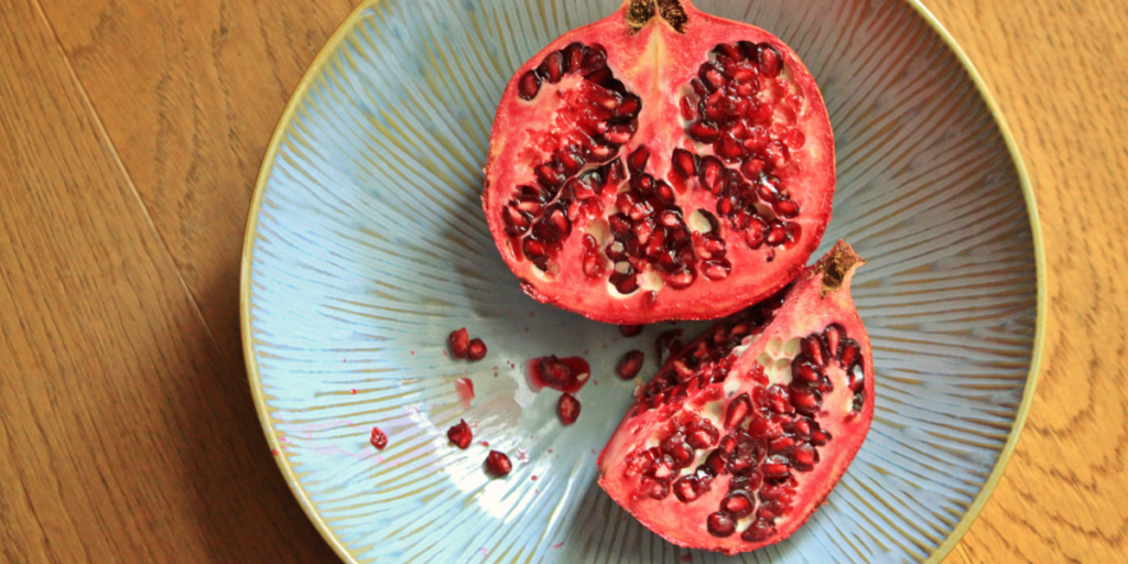 Freshly halved pomegranate with ruby-red arils on a blue ceramic plate, used as a natural ingredient for DIY red hair dye