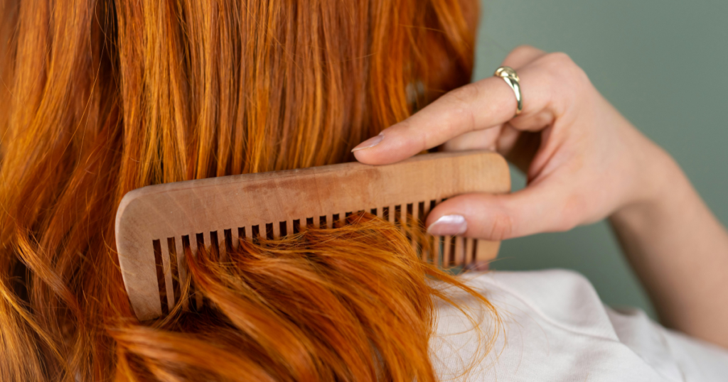 A woman combing through vibrant red hair with a wooden wide-tooth comb, showcasing rich copper tones before a natural hair dye removal treatment