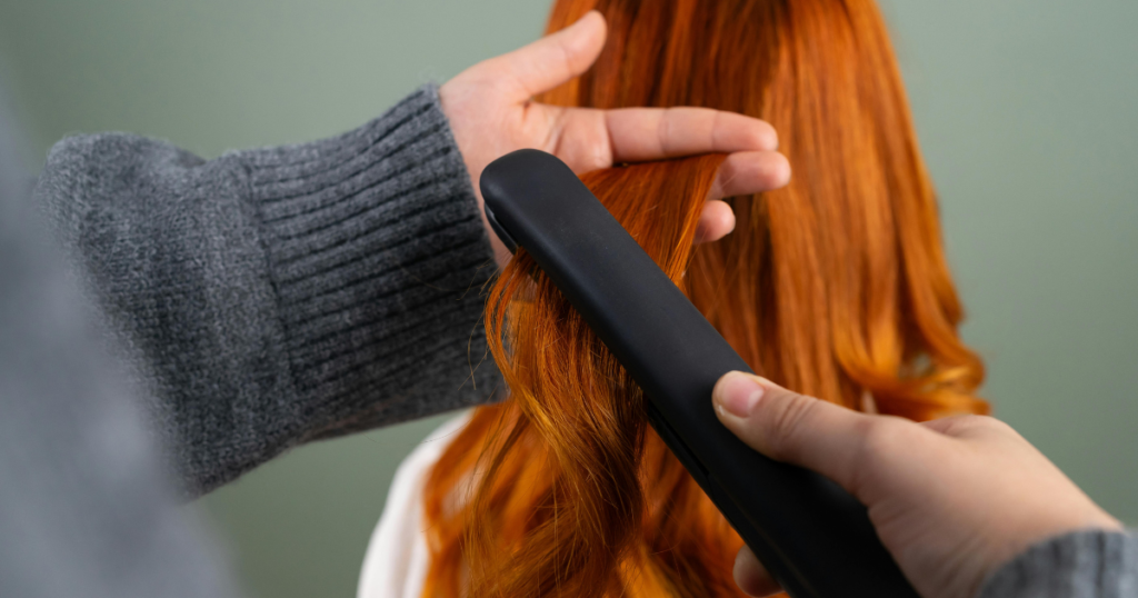 Close-up of a hairstylist straightening long, flowing red hair with a flat iron, highlighting the warm tones of a natural homemade red hair dye
