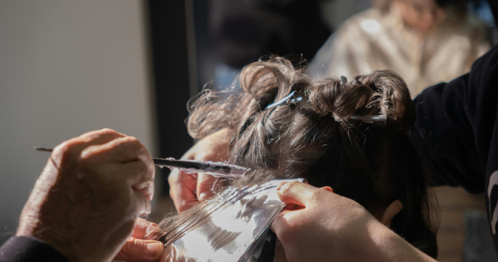 Close-up of a stylist painting hair color onto foil-wrapped sections of dark brown hair, demonstrating a professional coloring technique