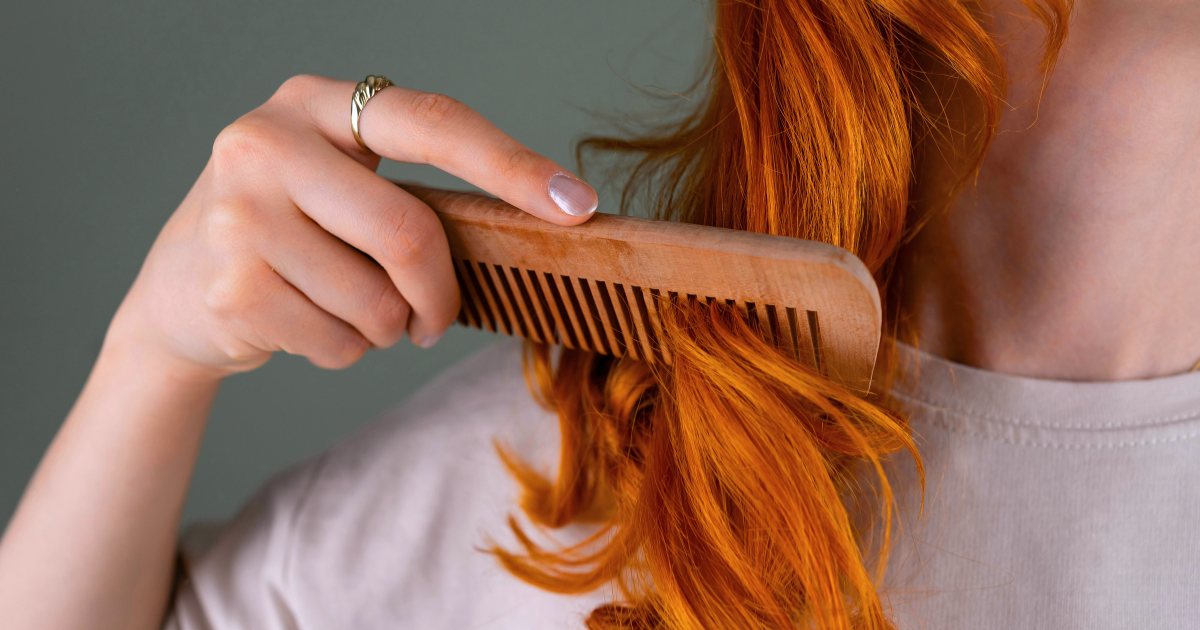 Woman combing long, vibrant red hair with a wooden comb, showcasing naturally dyed hair color results