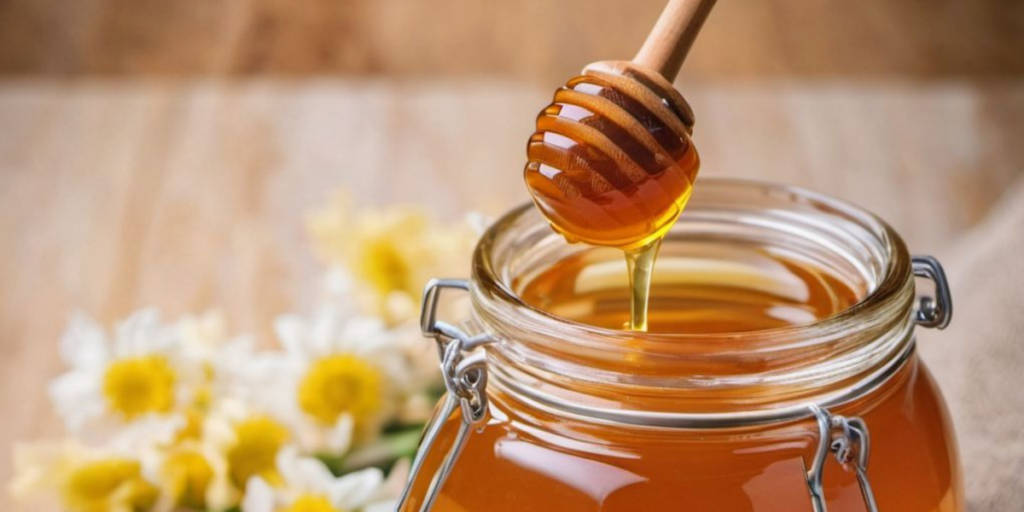 A glass jar of raw honey with a wooden honey dipper drizzling golden honey, a natural home ingredient for gradually fading red hair dye