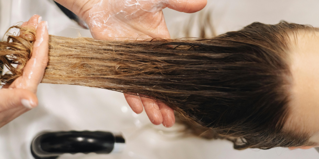 Hands rinsing natural black hair dye from dark hair at a salon sink, showing the correct rinsing technique after a home dye treatment