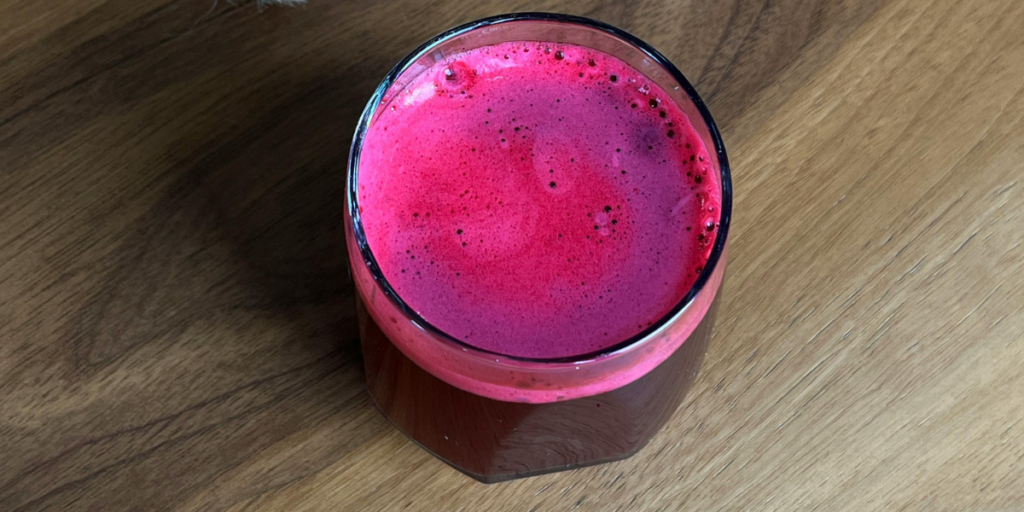 A glass of vibrant deep pink beetroot juice on a wooden surface, showing the rich cherry-red pigment used as a natural hair dye ingredient