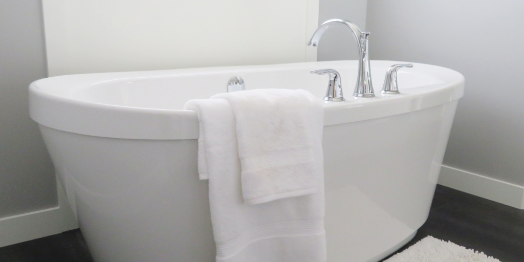 A clean white freestanding bathtub with chrome faucets and a white towel draped over the side, showing the porcelain surface that can stain from black hair dye.