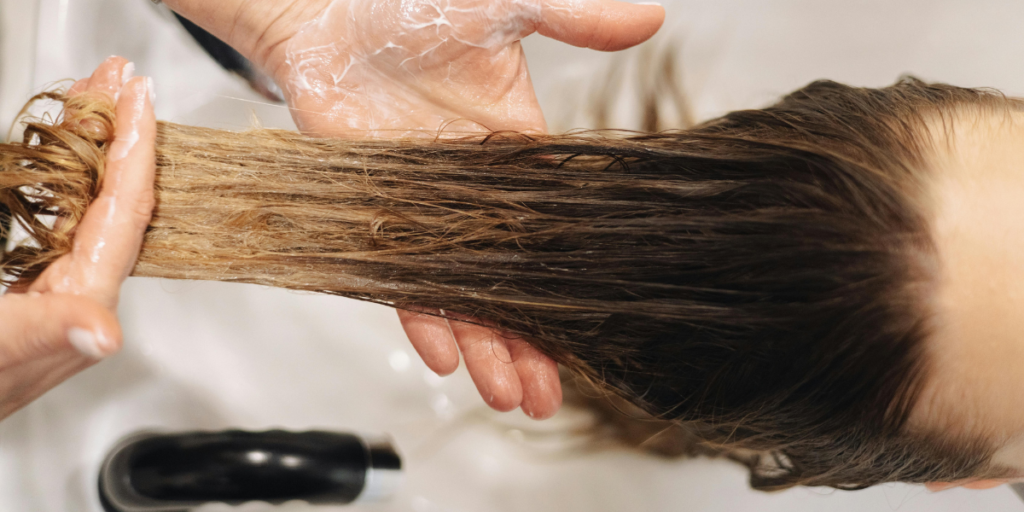 Stylist rinsing black hair dye from a client's hair at a salon basin, showing how washing affects color longevity